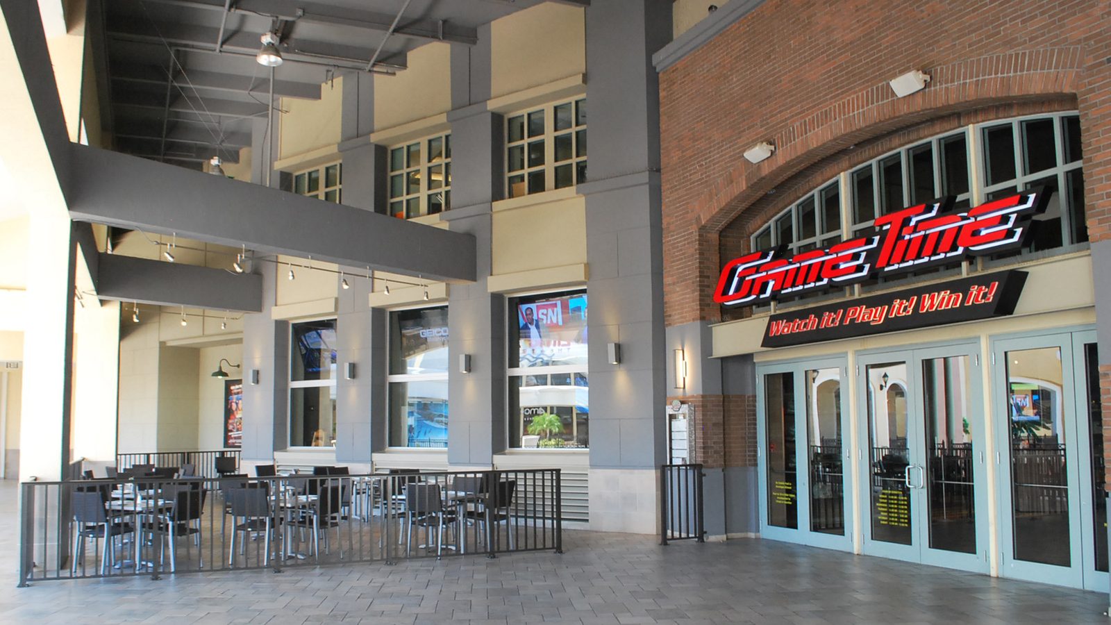 The outside of GameTime Miami: a brick arch with the red GameTime sign over the glass doors, patio tables under the covered walkway beside it